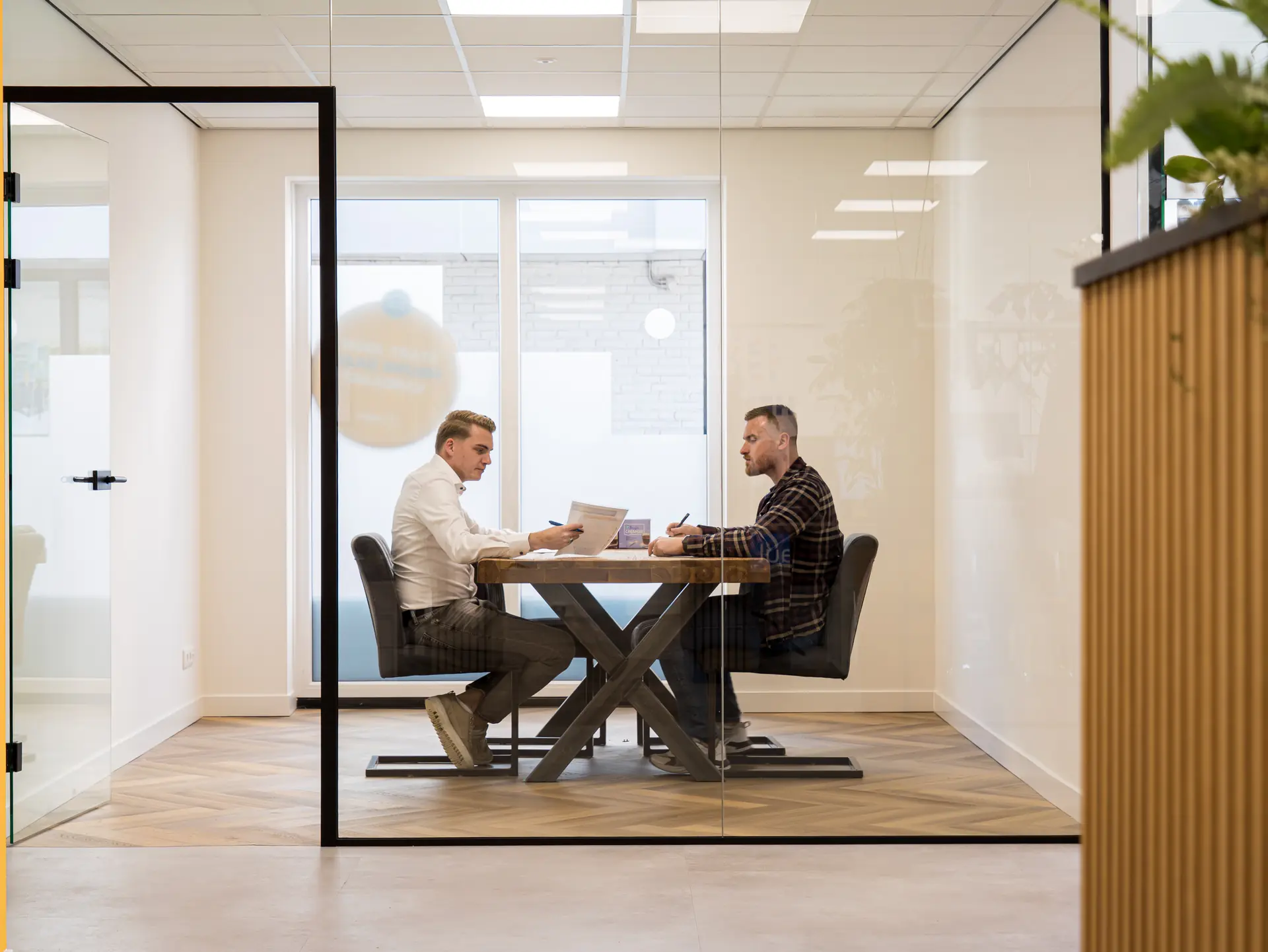 Twee mensen in gesprek aan tafel in een spreekkamer van HENK detachering